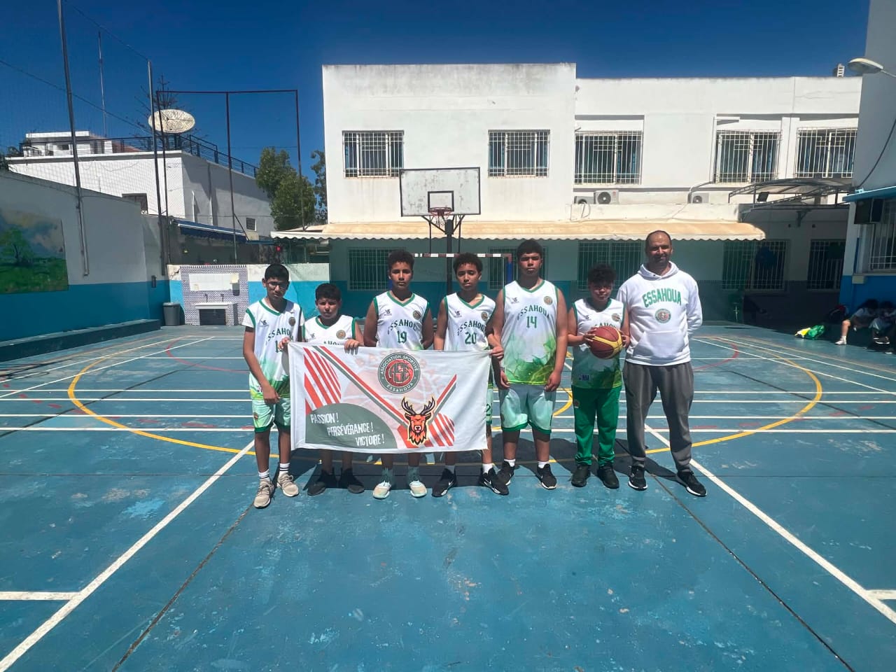 Équipe de jeunes joueurs et leur coach avec la banderole du club sur le terrain extérieur
